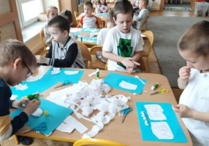 Dzieci wykonują prace plastyczną. Komponują biały świat na kartce niebieskiego koloru.