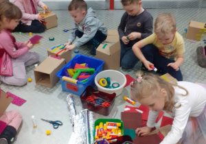Dzieci tworzą z kartonowych pudełek papierowe domy według własnego pomysłu.