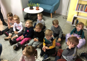 Dzieci siedzą na podłodze i słuchają czytanego opowiadania.