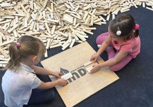Dwie dziewczynki układają budowlę z drewnianych klocków.