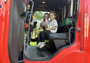 Dzieci siedza w kabinie wozu strażackiego.