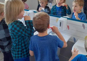 Chłopcy w łazience szczotkują zęby pod baczną kontrolą studentów.