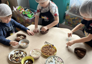 Dzieci z grupy jeżyków ozdabiają czekoladowe serca sładkimi dodatkami.