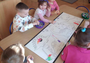 Dzieci z grupy Żabek koloruja dinozaury.